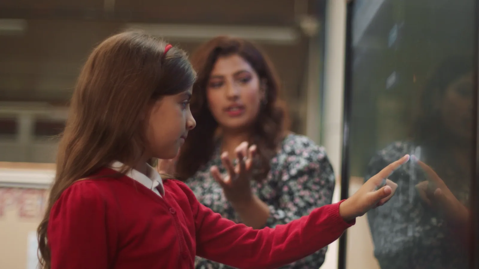A pupil working at the classroom board as Noni looks on