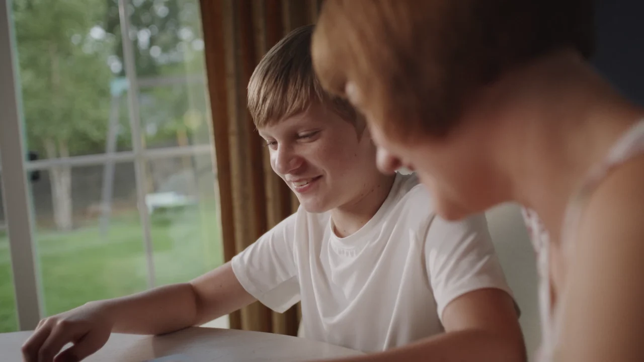 Silas smiling while using the laptop beside Kelly